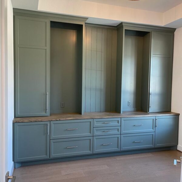 Built-in cabinetry with greenish-gray cabinets and drawers, wooden countertop, and silver handles creates a fresh look for your kitchen renovation, set against a light-colored wall with a modern ceiling light above.