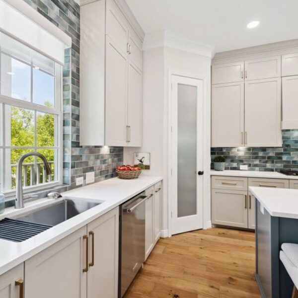Modern kitchen with white cabinets, blue-gray tile backsplash, stainless steel sink, and island.
