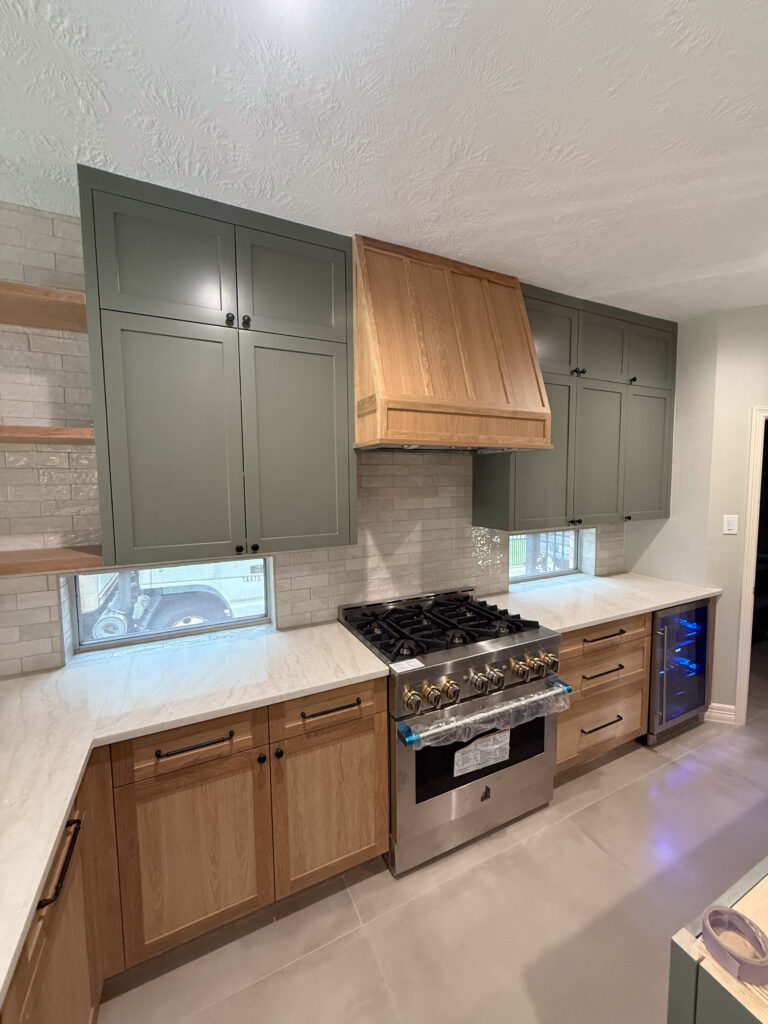 Kitchen with stainless steel gas stove, wood range hood, green upper cabinets, wood lower cabinets, light countertops, gray tile backsplash, and beverage cooler.