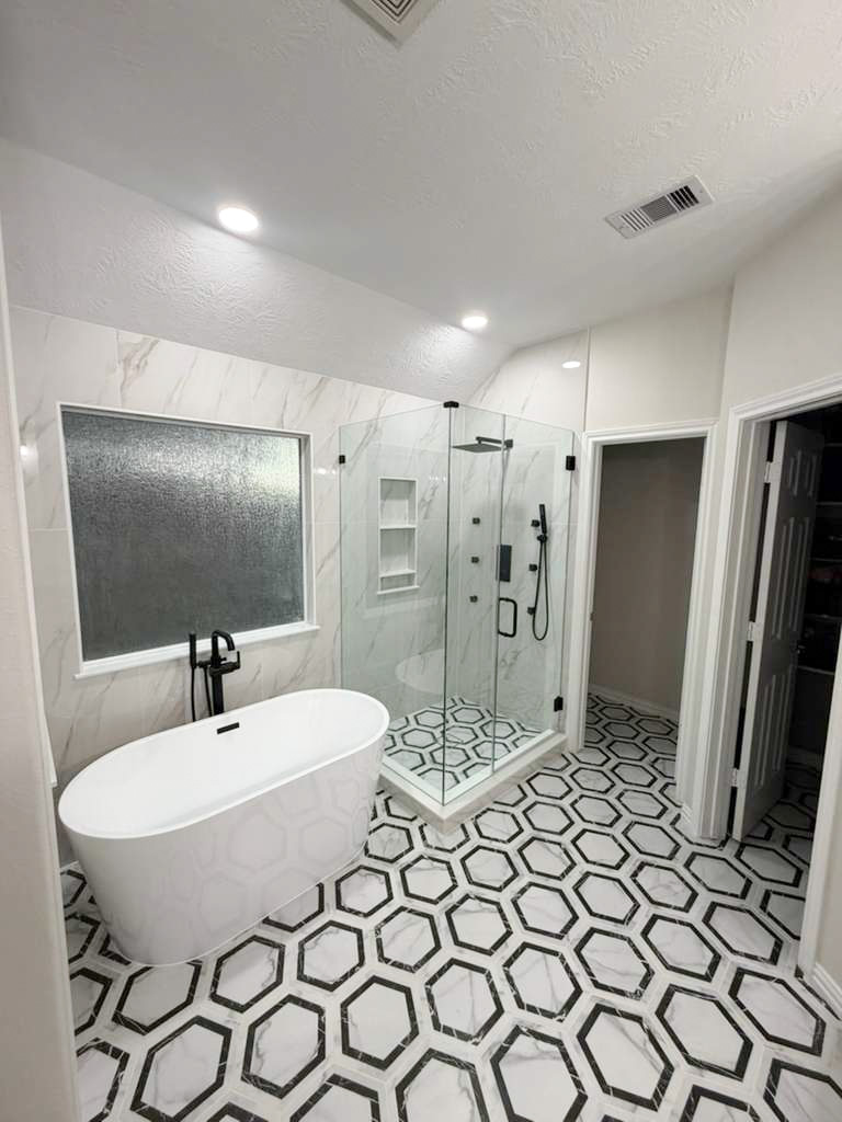 A bathroom featuring a white freestanding tub, a glass-enclosed shower, and white and black hexagonal floor tiles.